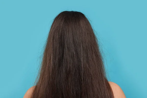 Woman with damaged hair before treatment on light blue background, back view