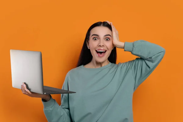Surprised woman with laptop on orange background