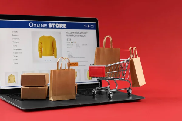 Online store. Laptop, mini shopping cart and small purchases on red background