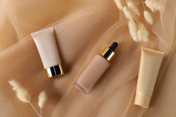 Skin foundation and dried reeds on beige tulle fabric, flat lay. Makeup product