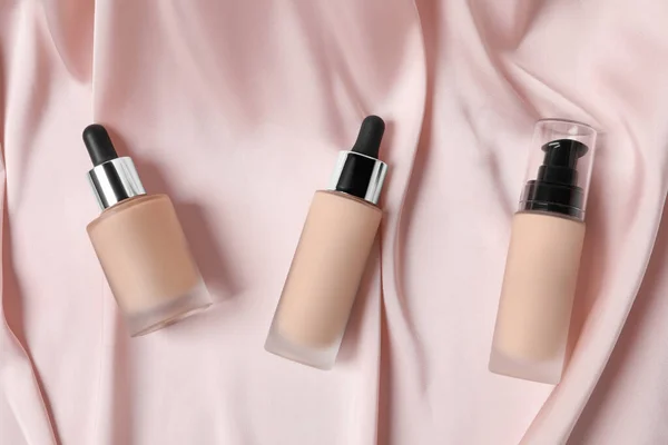 Bottles of skin foundation on pink cloth, flat lay. Makeup product