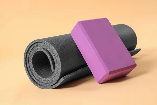 Grey exercise mat and yoga block on beige background