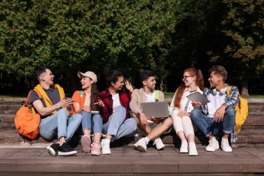 Bir grup mutlu genç öğrenci parkta birlikte öğreniyor.