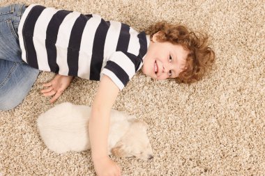 Bej halıda şirin köpek yavrusu olan küçük bir çocuk.