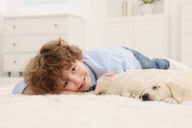 Evdeki beyaz halıda sevimli köpek yavrularıyla uzanan küçük çocuk.