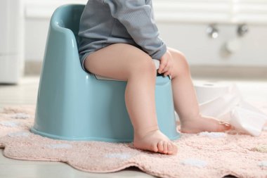 Küçük çocuk içeride plastik bebek tuvaletinde oturuyor, yakın plan.