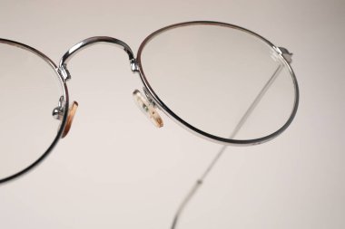 Bej arka planda metal çerçeveli şık bir gözlük, yakın plan.