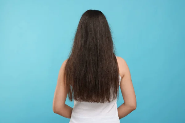 Woman with damaged hair before treatment on light blue background, back view