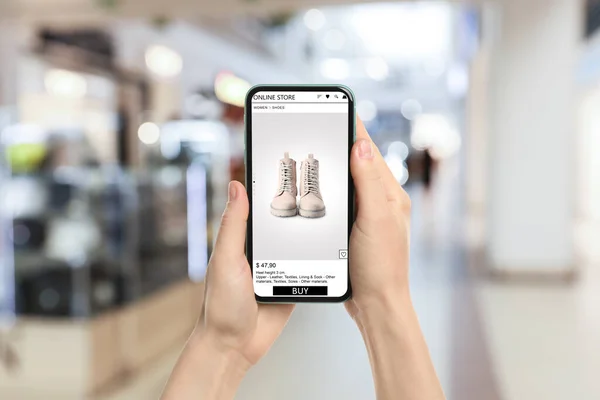 Woman visiting shop to take ordered boots indoors, closeup. Online store website on device screen