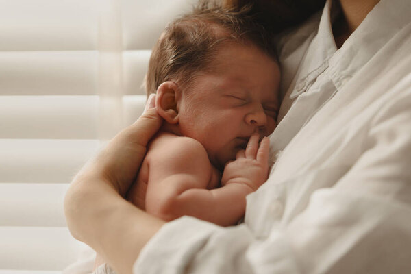 Mother holding her cute newborn baby indoors, closeup