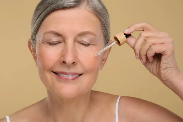 Seniorin Trägt Kosmetikprodukt Auf Ihre Alternde Haut Vor Beigem Hintergrund — Stockfoto
