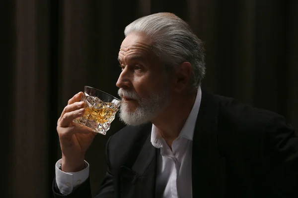 Senior man in suit drinking whiskey on black background