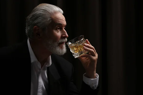 Senior man in suit drinking whiskey on black background