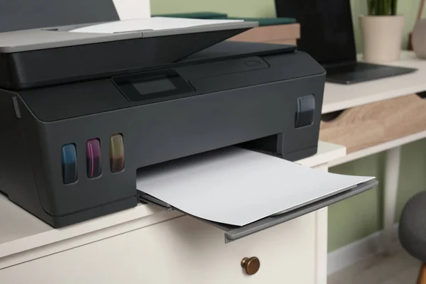 Modern printer with paper on white chest of drawers indoors, closeup