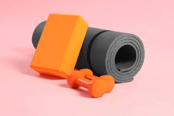 Grey exercise mat, yoga block and dumbbells on pink background