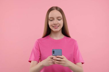 Mutlu genç kadın pembe arka planda akıllı telefon kullanıyor.