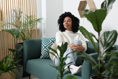 Rahatlatıcı atmosfer. Evdeki güzel çiçeklerin yanındaki kanepede oturan kadın.