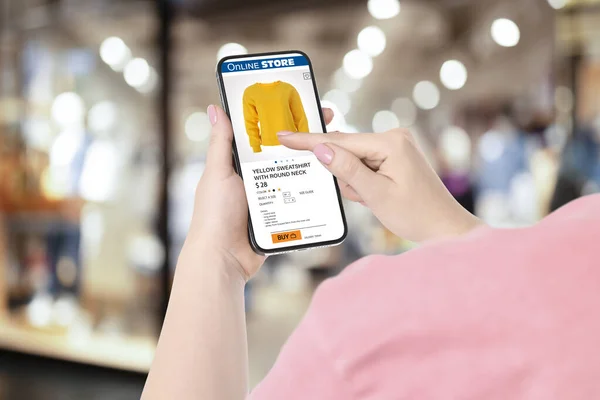 Woman visiting shop to take ordered sweatshirt indoors, closeup. Online store website on device screen