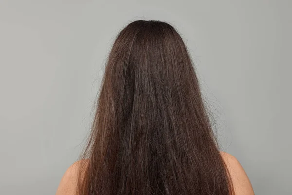 Woman with damaged hair before treatment on light grey background, back view