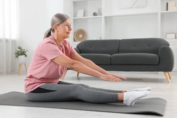 穿着运动服的老年妇女在家里的健身垫上伸懒腰 — 图库照片