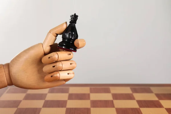 Robot with chess piece above board against light background, space for text. Wooden hand representing artificial intelligence
