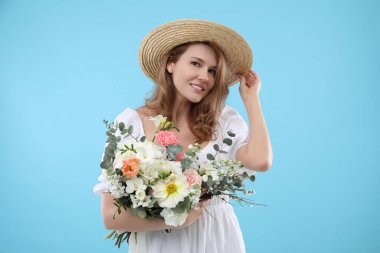 Hasır şapkalı güzel bir kadın açık mavi arka planda bir buket çiçekle