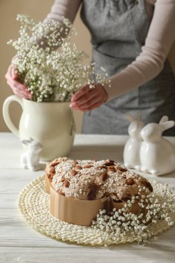 Lezzetli İtalyan Paskalya pastası (geleneksel Colomba di Pasqua). Beyaz ahşap masaya buket koyan kadın.