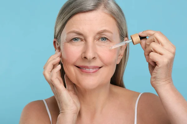 Senior Woman Applying Cosmetic Product Her Aging Skin Light Blue — Stock Photo, Image