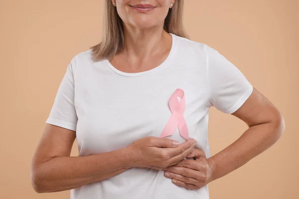 Breast cancer awareness. Woman with pink ribbon doing self-examination on light brown background, closeup