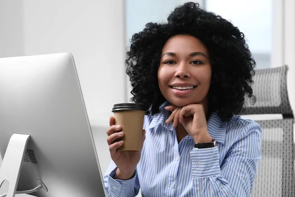 Young woman with cup of drink working on computer in office