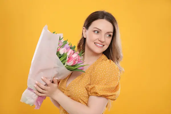 黄色の背景に美しいチューリップの花束を持つ幸せな若い女性 — ストック写真
