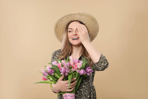 幸せな若いです女性でわら帽子保持花束の美しいですチューリップオンベージュ背景 — ストック写真