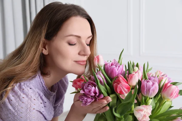Woman smelling bouquet of beautiful tulips indoors