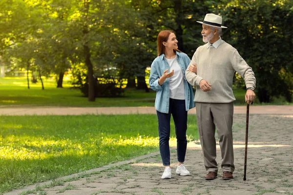 Senior man with walking cane and young woman in park. Space for text