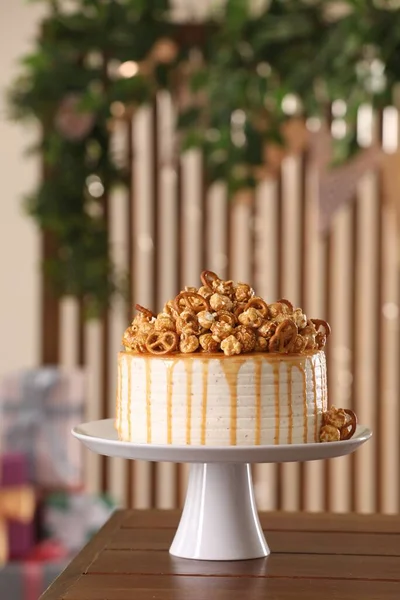 Caramel drip cake decorated with popcorn and pretzels on wooden table, space for text