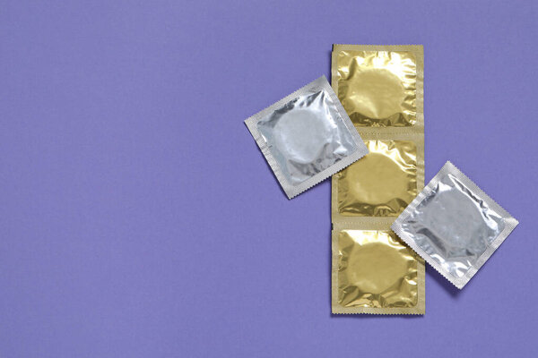 Пакеты презервативов на фиолетовом фоне, плоская раскладка и место для текста. Safe sex