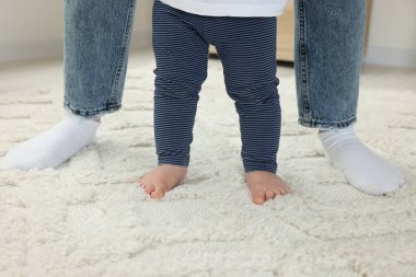 Anne oğluna destek oluyor. Halıda yürümeyi öğrenirken, yakın plan.