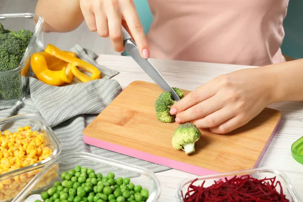 Woman cutting broccoli and glass containers with fresh products on white wooden table, closeup. Food storage