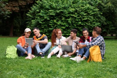 Bir grup mutlu genç öğrenci parktaki yeşil çimlerde birlikte öğreniyor.