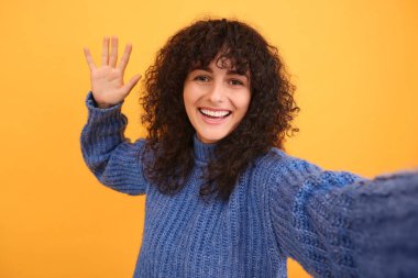 Güzel genç bir kadın turuncu arka planda selfie çekiyor.