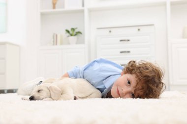 Evdeki beyaz halıda sevimli köpek yavrularıyla uzanan küçük çocuk.