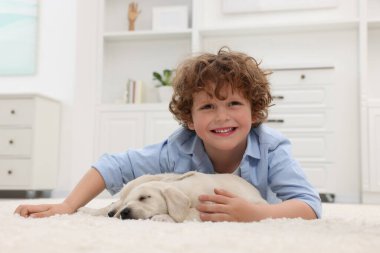 Evdeki beyaz halıda sevimli köpek yavrularıyla uzanan küçük çocuk.