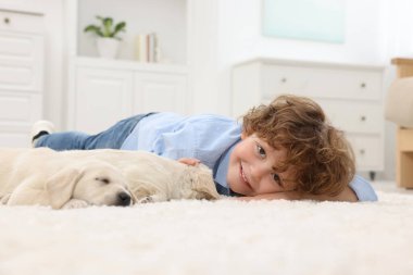 Evdeki beyaz halıda sevimli köpek yavrularıyla uzanan küçük çocuk.