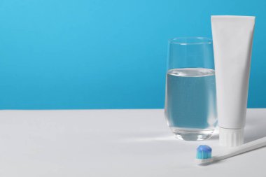 Açık mavi arkaplan, metin için boşluk, beyaz masa üzerinde yapıştırıcı ve bardak su ile plastik diş fırçası