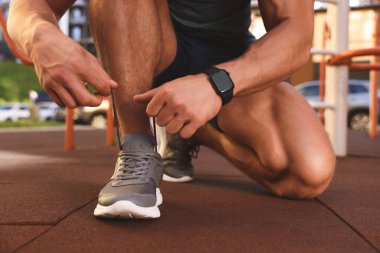 Spor salonunda antrenmandan önce ayakkabı bağcıklarını bağlayan adam, yakın plan.