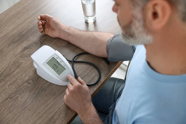 stock image Man measuring blood pressure at table indoors, closeup