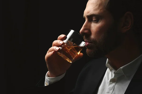 Man in suit drinking whiskey on black background