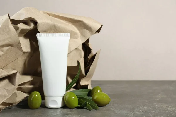 Tube of cream with olive essential oil and kraft crumpled paper on dark grey table. Space for text