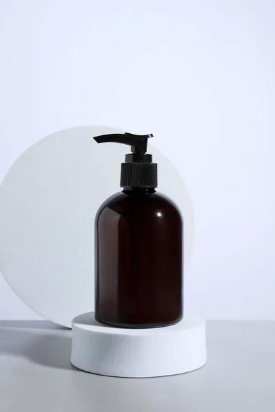 Bottle of cosmetic product and podiums on light grey table against white background