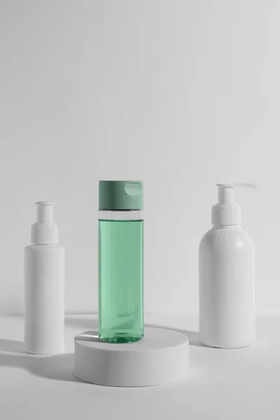 Bottles with different cosmetic products and podium on white background